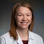 A white woman with short brown hair to her shoulders, parted on the left smiling and wearing a white doctors coat