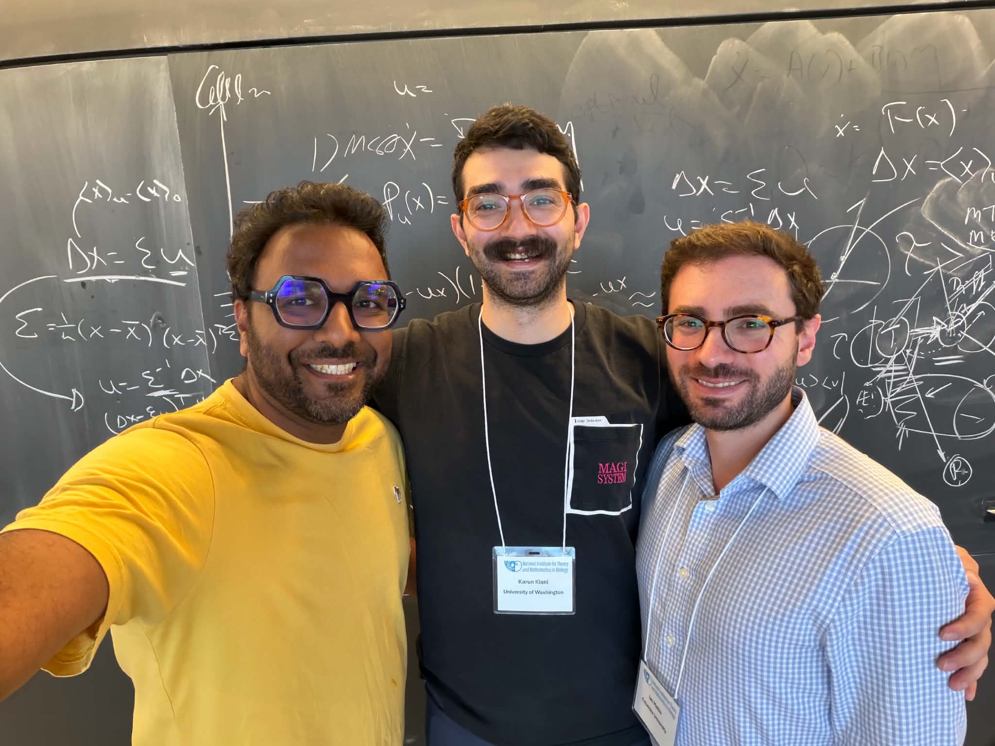 Three men smiling in front of a chalkboard
